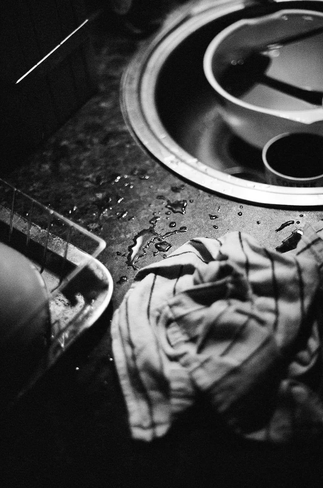 Black-and-white close-up of a dishwasher tub floor with standing water and debris around the drain