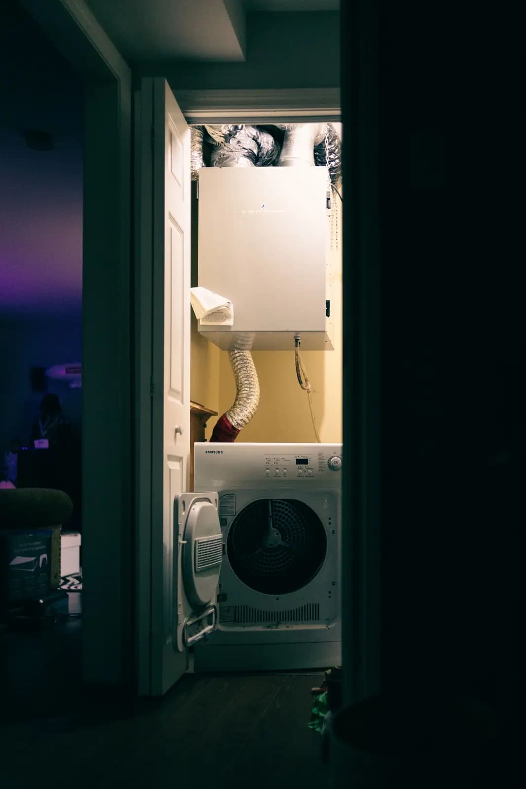 Stacked laundry closet with a foil dryer duct running up the wall behind the machines