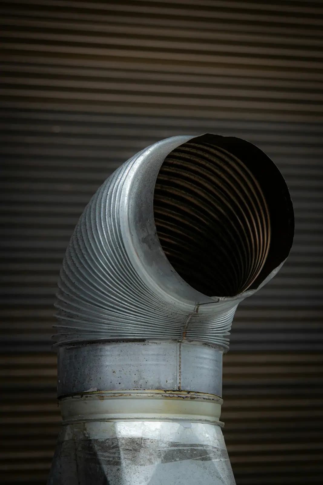 Close-up of a semi-rigid metal duct elbow against a wall