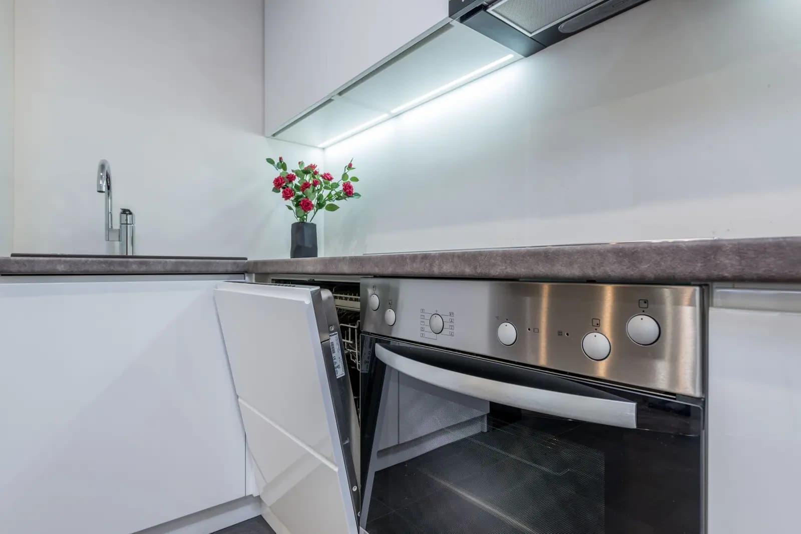 White kitchen with an open built-in dishwasher beside the wall oven