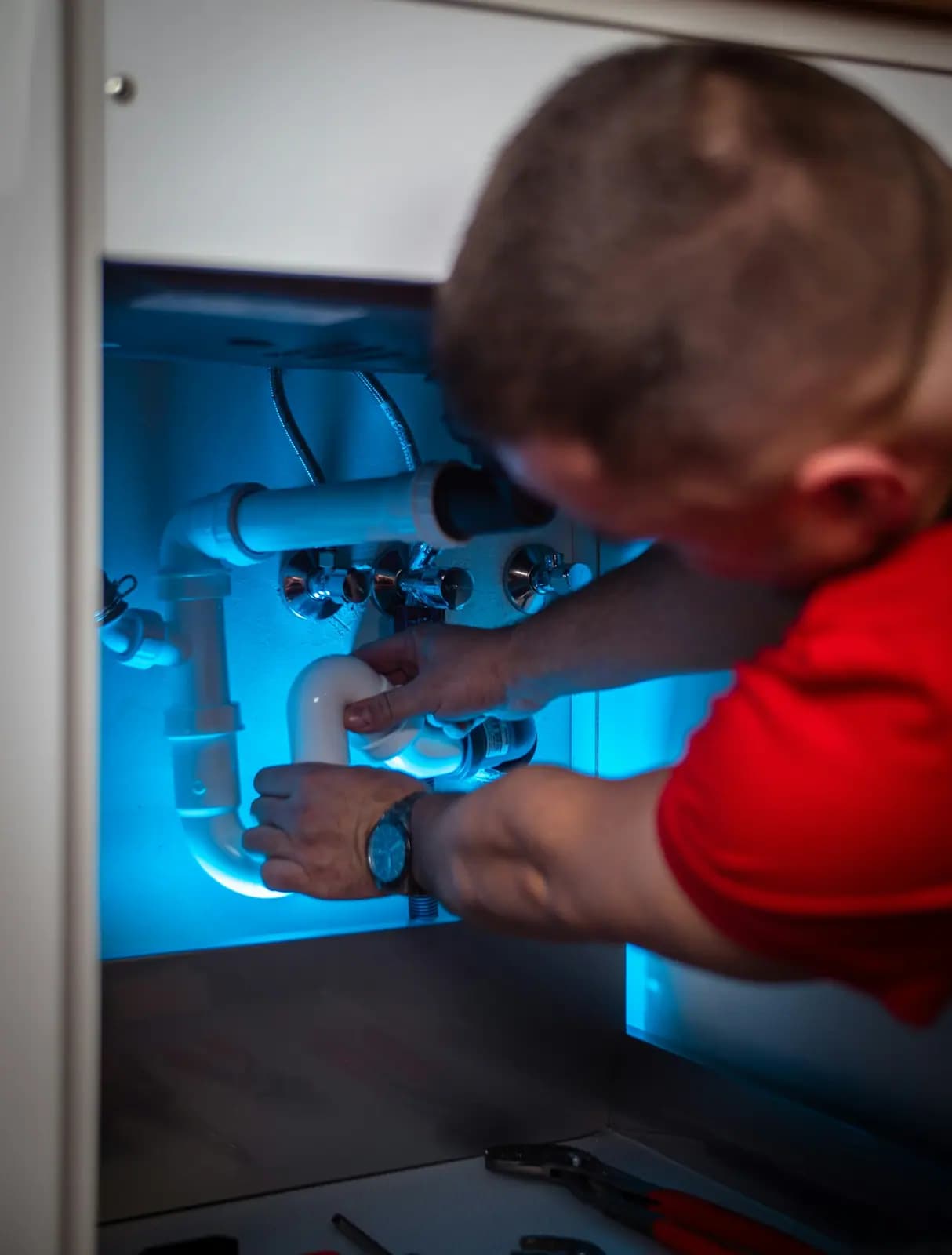 Person working on drain fittings inside an under-sink cabinet