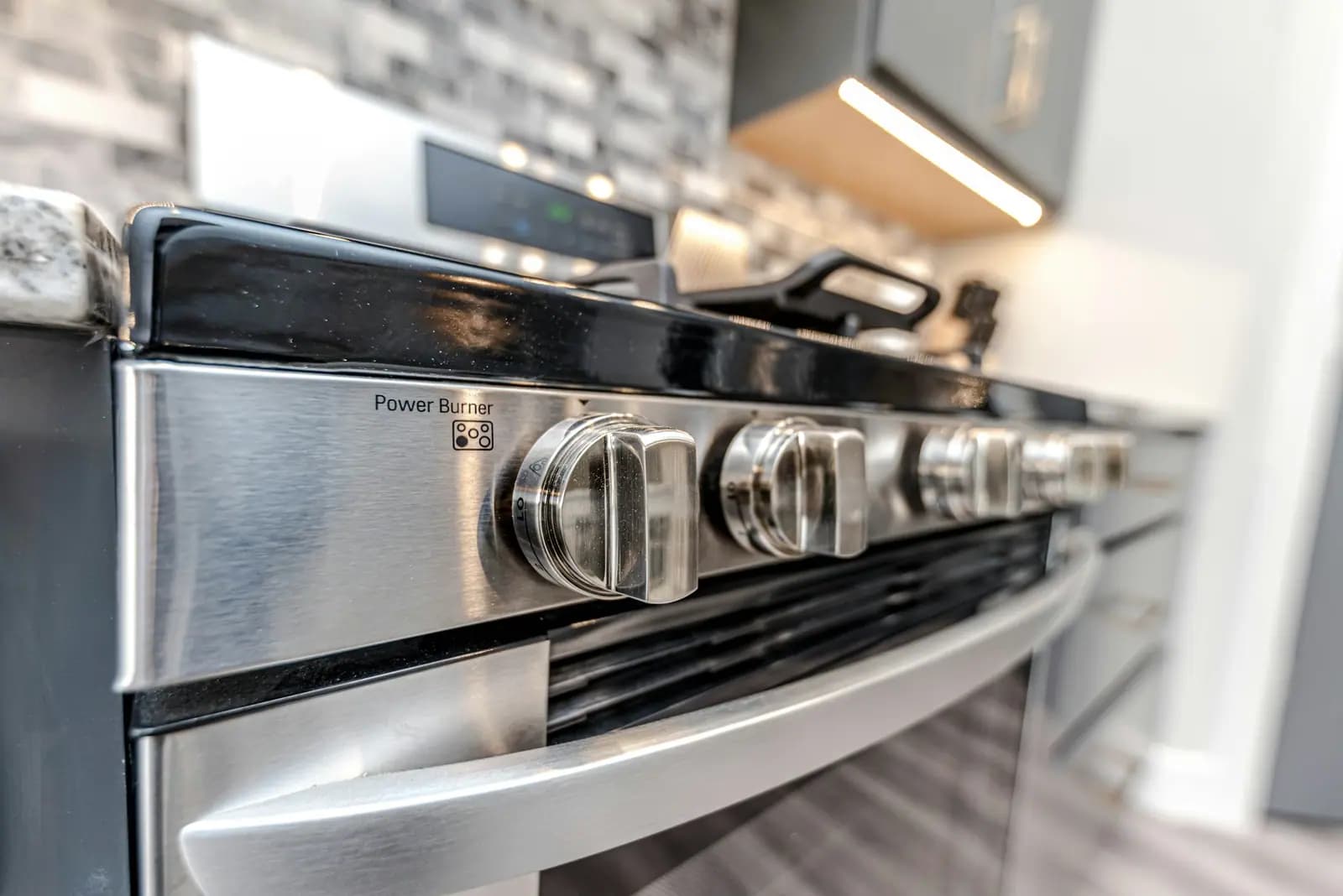 Stainless range with front knobs and oven door handle under cabinet lighting
