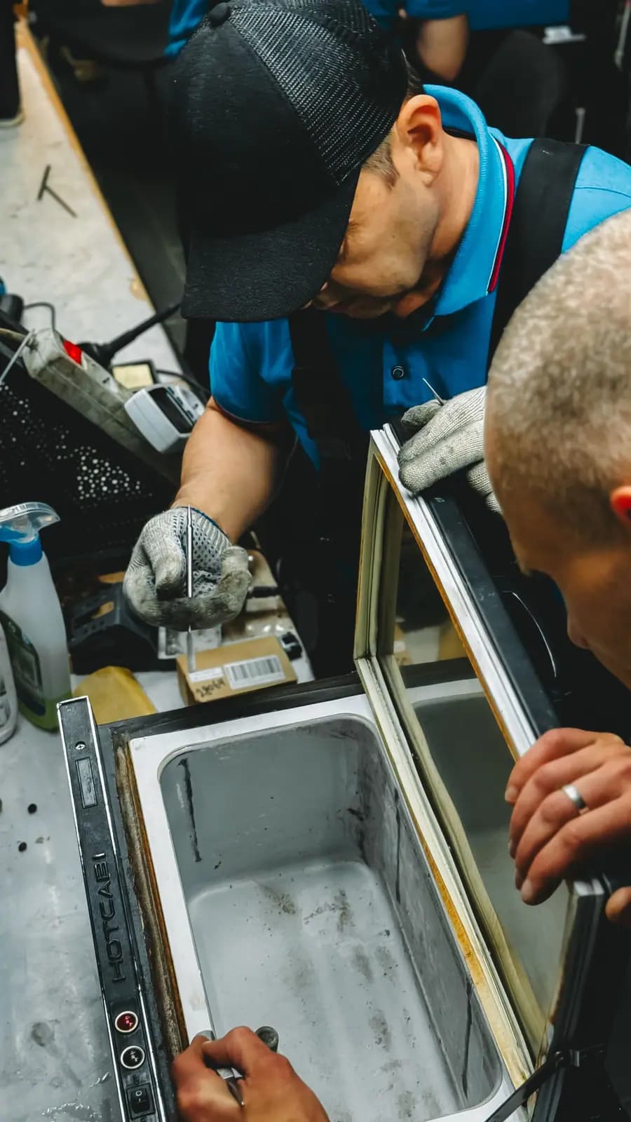 Two technicians in gloves working on the door frame of a glass-door freezer